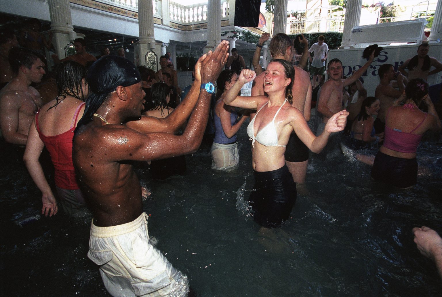 A couple having fun in a swimming pool, dancing, looking at eachother, smiling, surrounded by party pool people. Es Paradis, San Antonio Club 1830, Ibiza 2001. (Photo by Des Willie/PYMCA/Avalon/Getty Images)