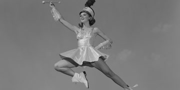 1960s WOMAN MAJORETTE HOLDING BATON WEARING SHORT SKIRT UNIFORM JUMPING INTO THE AIR  (Photo by H. Armstrong Roberts/ClassicStock/Getty Images)