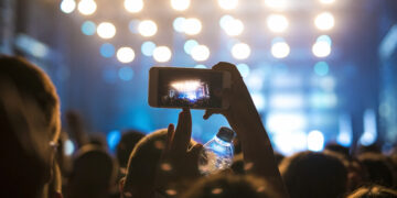 Woman in the crowd taking picture of stage at music festival.